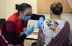 Une infirmière portant un masque vaccine une femme portant des tatouages sur le bras